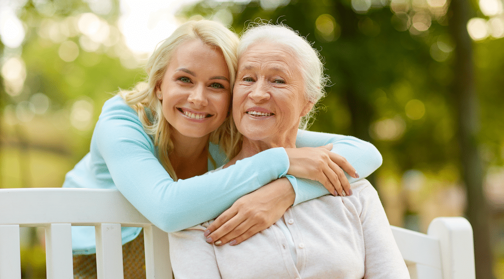 daughter with senior mother hugging on park bench